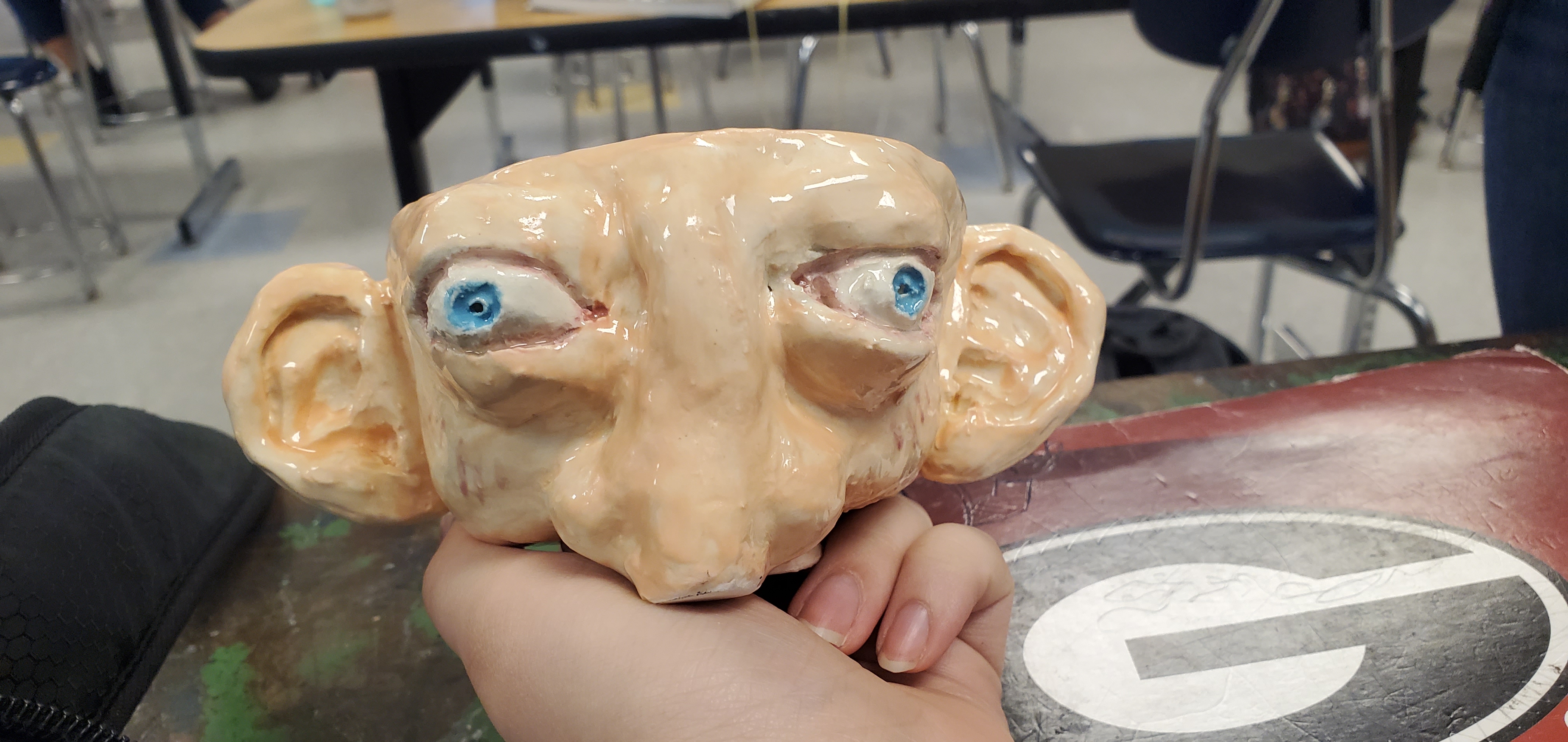 Handheld glazed ceramic sculpture combining several faces with blue eyes